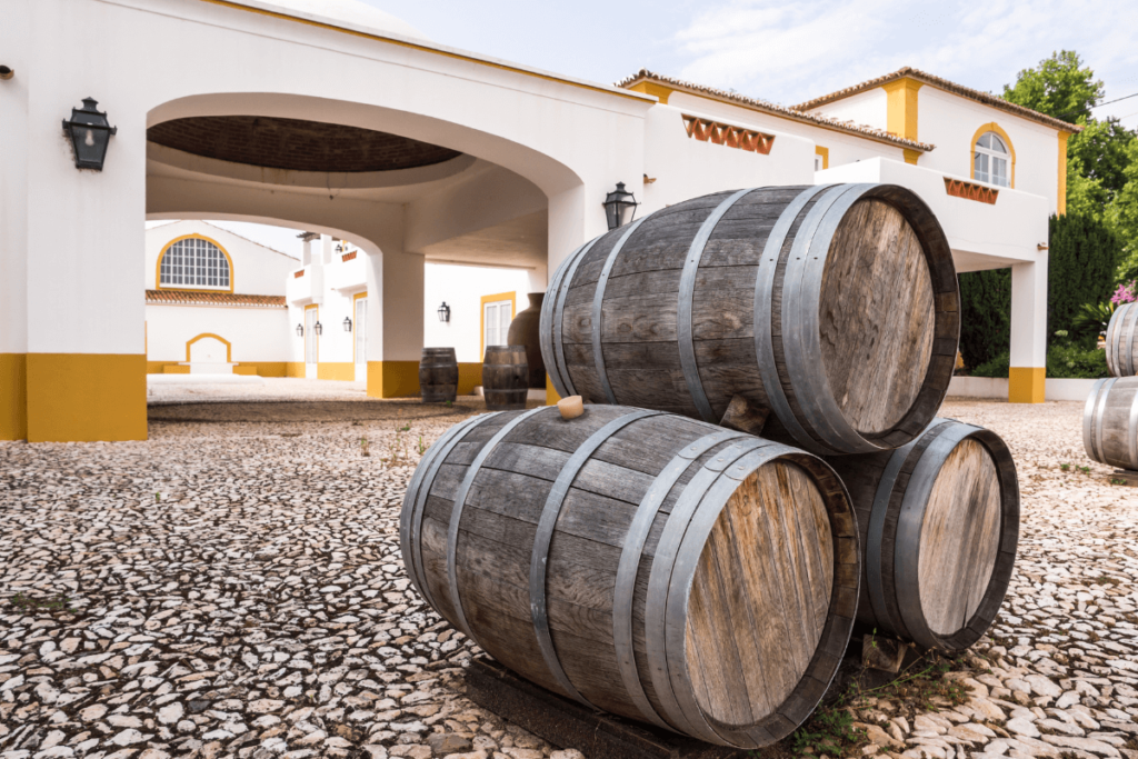 Barris de vinho de carvalho empilhados em frente a uma vinícola tradicional portuguesa no Alentejo, região conhecida por seus vinhos encorpados e complexos.