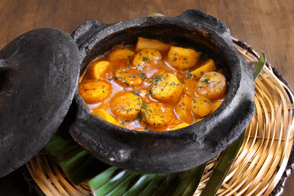 Uma panela de barro fumegante repleta de moqueca de banana da terra, um prato típico brasileiro que combina a doçura da banana com o sabor marcante do camarão em um caldo cremoso e aromático.