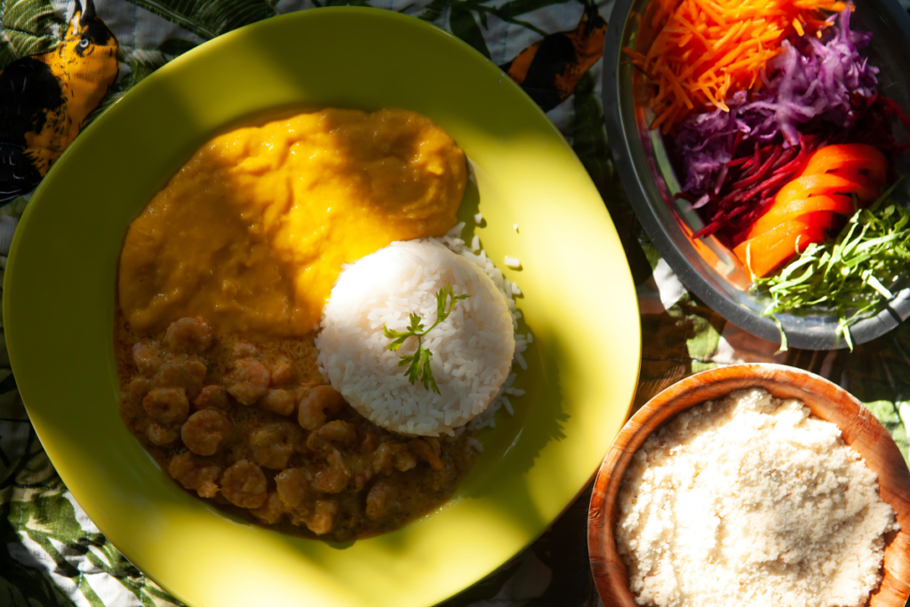 Um prato colorido e apetitoso da culinária baiana: moqueca de camarão cremosa acompanhada de arroz branco, pirão, farofa e uma salada fresca. Uma explosão de Sabores da Bahia!