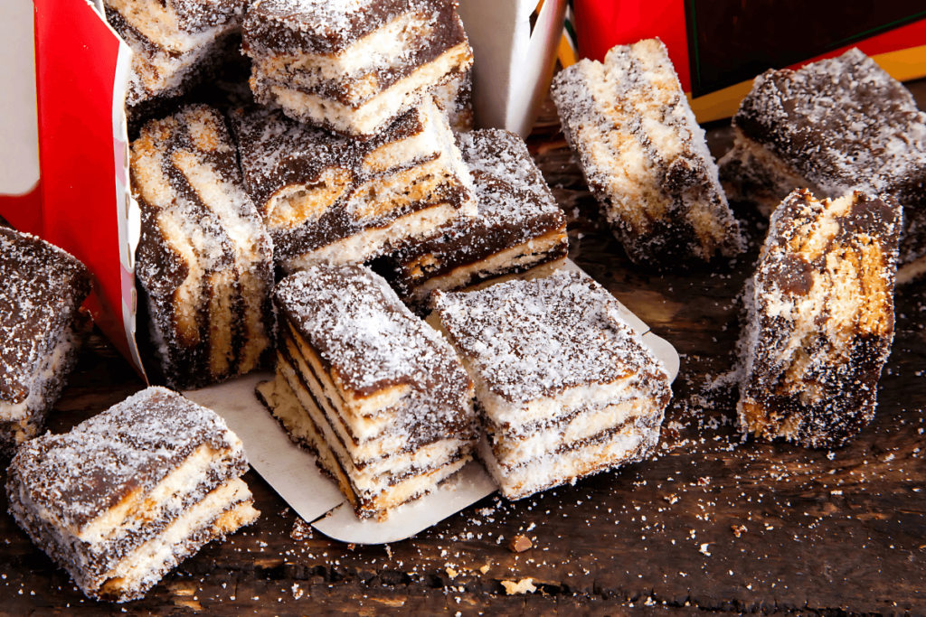 Cubos de palha italiana em camadas, com chocolate e biscoito, polvilhados com açúcar, em uma caixa de papel vermelha e branca sobre mesa de madeira, mostrando a tradição do doce brasileiro com história.