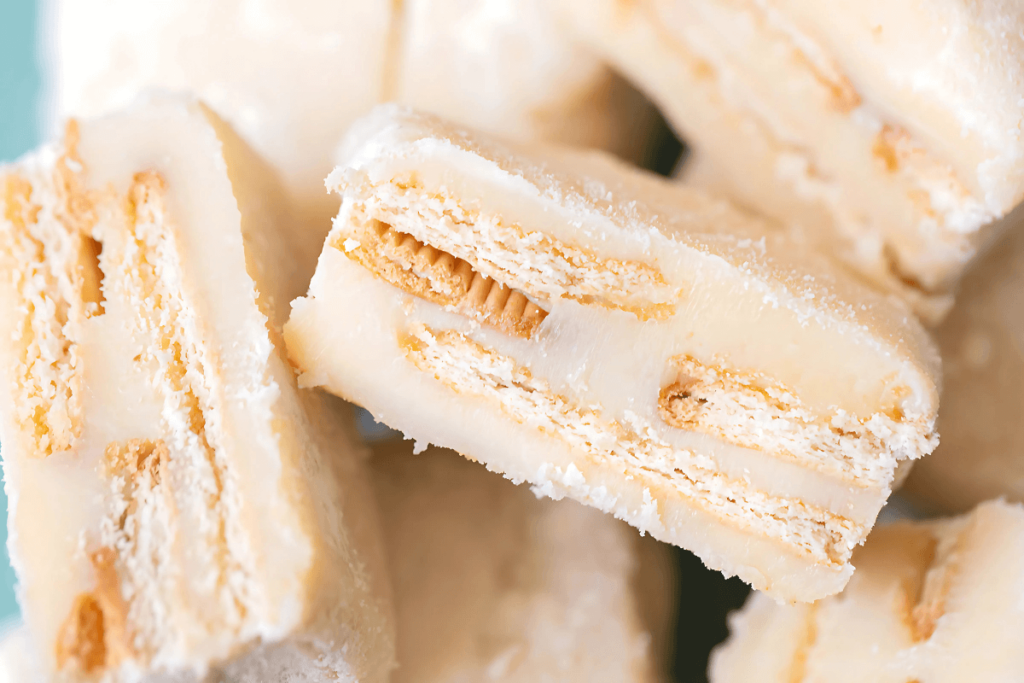 Close-up de cubos de palha italiana branca, com camadas visíveis de biscoito, textura cremosa e polvilhada com açúcar, mostrando uma variação do doce brasileiro com história.