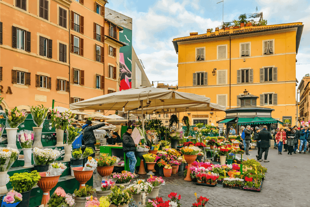Vista vibrante do Mercado Campo de' Fiori em Roma, as barracas e pessoas passeando, representando a atmosfera animada e a cultura gastronômica do Centro da Itália.