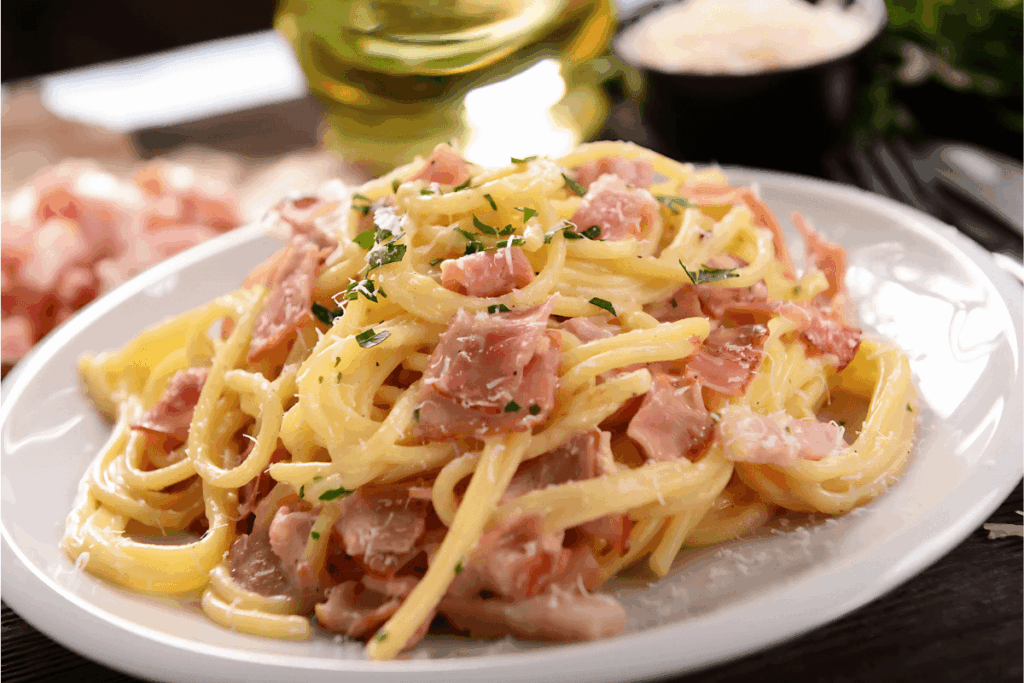 Close-up de um prato de Spaghetti alla Carbonara, um prato clássico da Gastronomia do Centro da Itália, com massa envolvida em molho cremoso, pedaços de guanciale crocante e queijo ralado, pronto para ser saboreado.