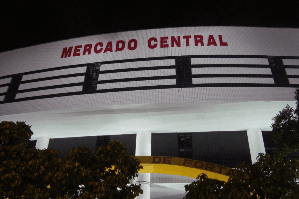 Fachada iluminada do Mercado Central de Fortaleza, Ceará, à noite, mostrando a arquitetura do prédio e a placa com o nome.