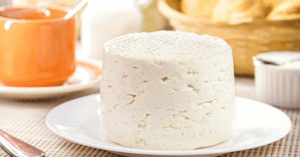 Peça de Queijo Minas Frescal branco, ícone da culinária de Minas Gerais, em um prato sobre uma mesa de café da manhã.